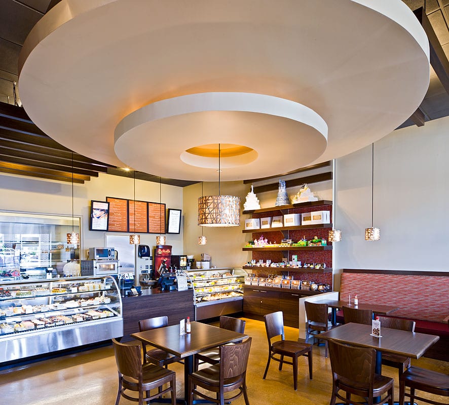 IndAroma’s pastry counter — a long refrigerated case of cake slices, a second case of pastries, the coffee station and tiered display cakes on the red mosaic shelf.