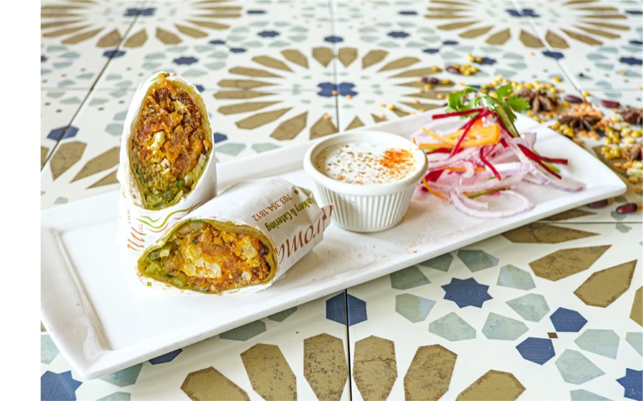 An IndAroma Kati roll, sliced and served with raita and pickled onions.